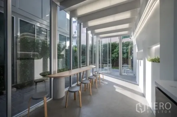 零售空间 出租在Khlong Toei, Bangkok - 店内采光充足，整面落地窗、长木吧台与高脚凳，面向绿篱