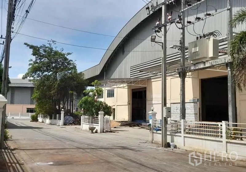 โรงงาน ให้เช่าในMueang Samut Prakan, Samut Prakan - ทางสัญจรด้านข้างอาคารโรงงาน มีประตูม้วน รั้ว และเสาไฟฟ้า