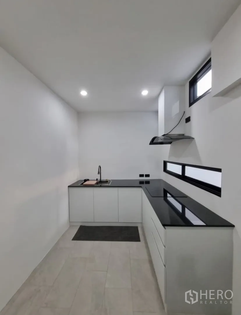 Detached House for rent in Suan Luang, Bangkok - Modern L-shaped kitchen with black stone countertops, sink, hob and slim windows.
