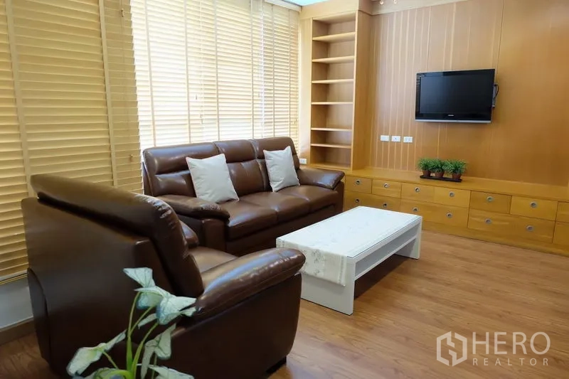 Condominium for rent in Khlong Toei, Bangkok - Cozy living room featuring brown leather sofa, TV, built-in cabinetry and coffee table