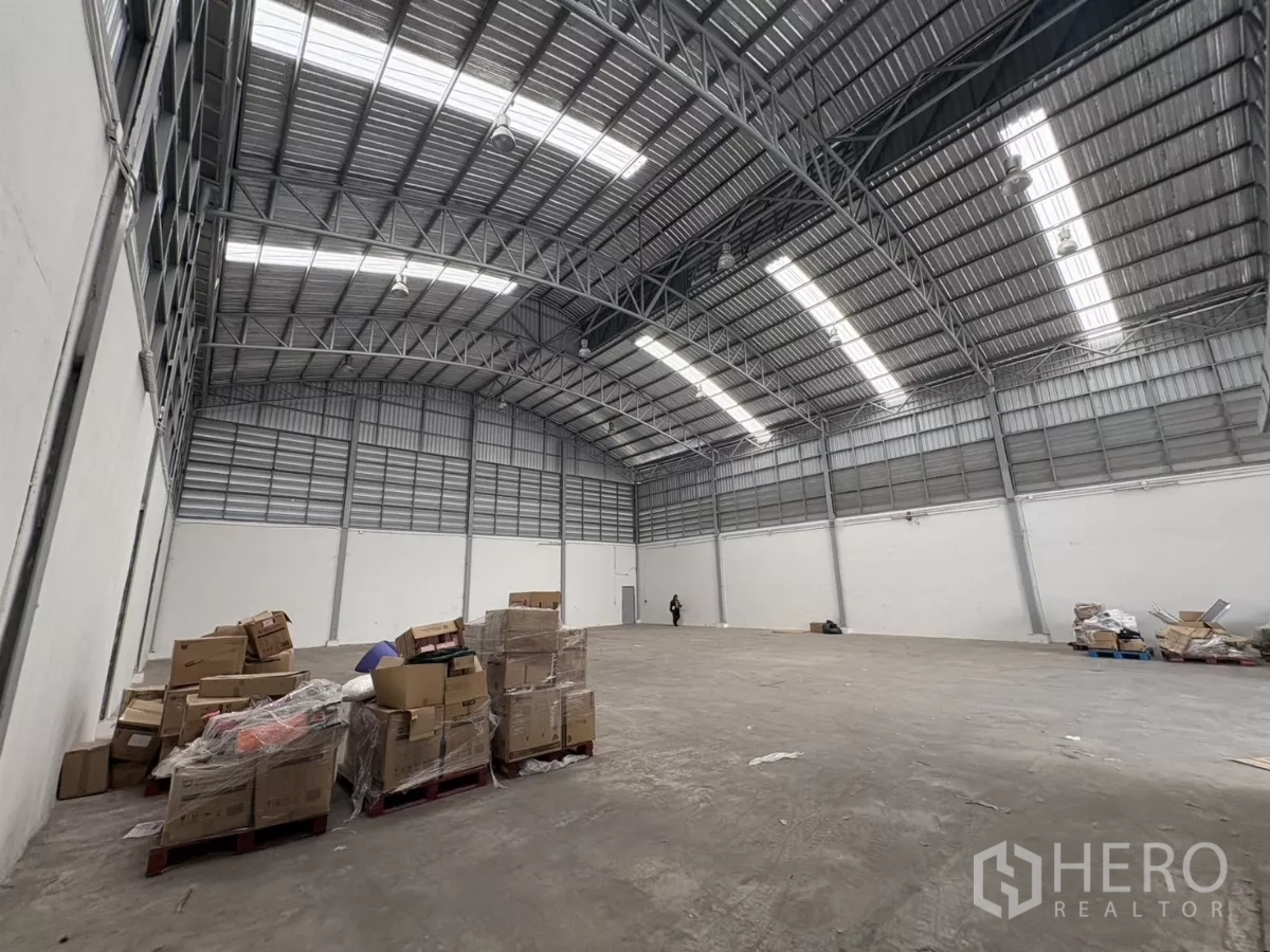 Warehouse for rent in Bang Phli, Samut Prakan - Open warehouse floor with high roof trusses and stacked pallets along the wall.