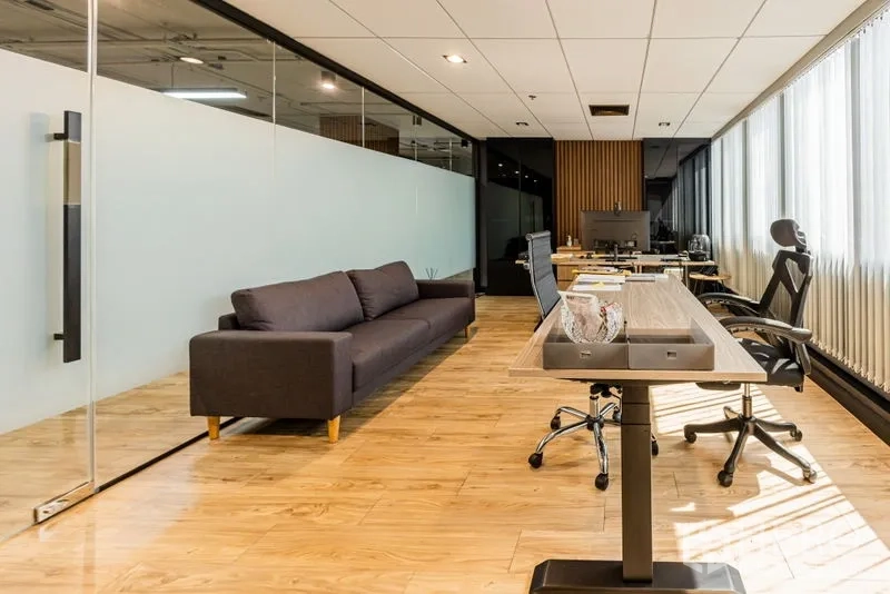 Office Space for rent - Glass-partitioned workspace with sofa, long bench desks and natural light.
