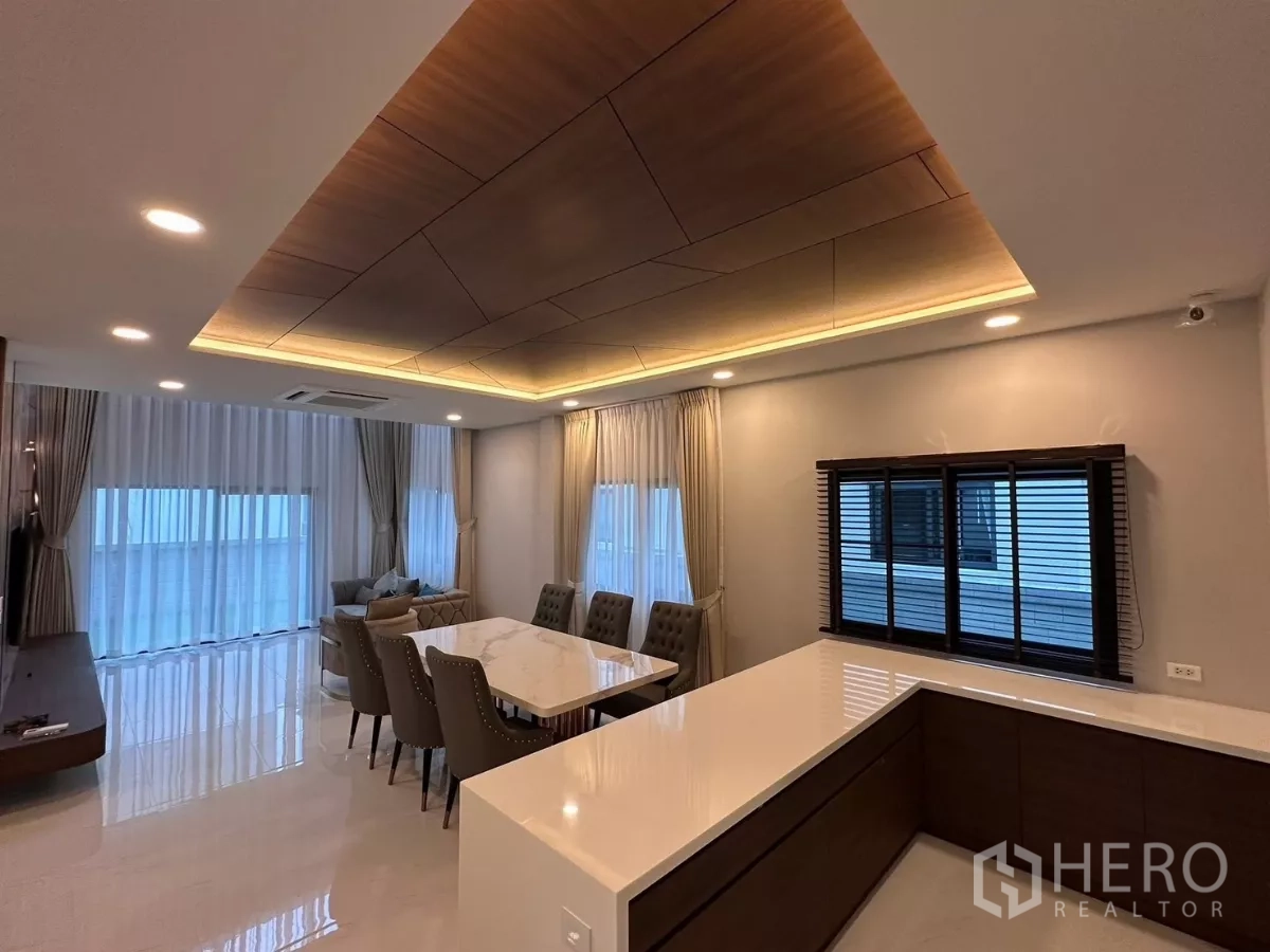 Detached House for rent in Bang Phli, Samut Prakan - Open-plan dining and kitchen with marble-top table, island counter, and coffered wood ceiling with LED lighting.
