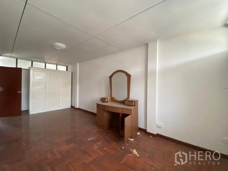 联排别墅 出租在Watthana, Bangkok - 宽敞卧室，拼花木地板、白墙，配衣柜与梳妆台。