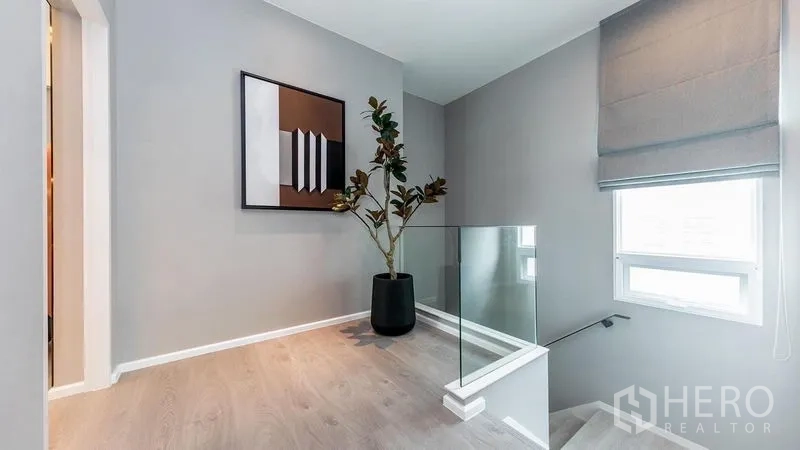 Detached House for rent in Prawet, Bangkok - Upstairs landing with glass balustrade, artwork and side window for daylight.