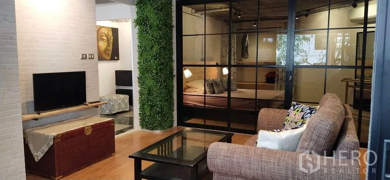 公寓 出售在Watthana, Bangkok - 开放式客厅与卧室，黑框玻璃隔断，电视与立体绿植墙。