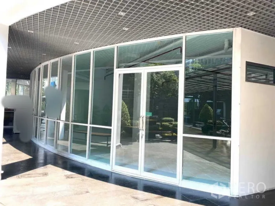 办公空间 出租在Khlong Toei, Bangkok - 弧形外立面玻璃与双开玻璃门，通向带绿化与遮荫的办公楼中庭。