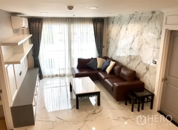 公寓 出租或出售在Khlong Toei, Bangkok - 采光充足的客厅，L型棕色皮沙发、仿大理石地面与落地窗帘。