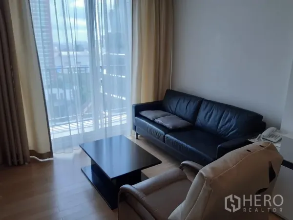 คอนโด ให้เช่าในKhlong Toei, Bangkok - ห้องนั่งเล่นสว่าง โซฟาหนังสีดำ เก้าอี้เอนนอน โต๊ะกลาง เปิดออกสู่ระเบียงพร้อมวิวเมืองและผ้าม่านโปร่ง