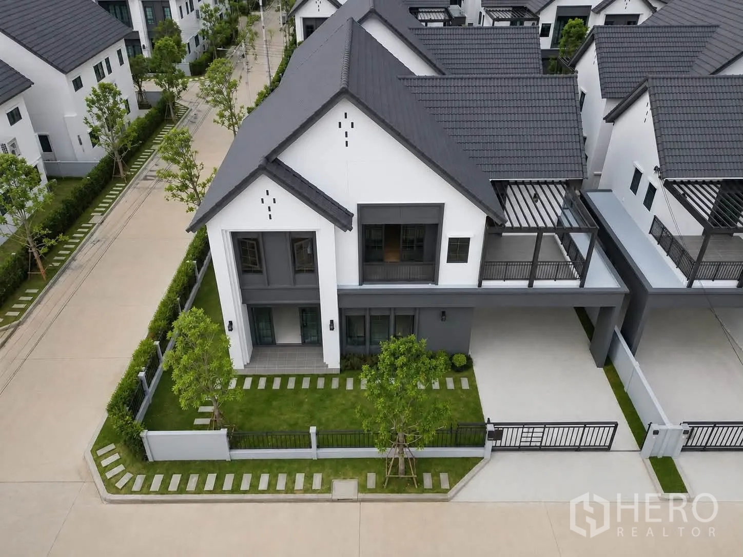 独栋房屋 for rent in Bang Phli, Samut Prakan - 转角地块的现代两层独栋别墅航拍图，带草坪、围栏和有顶车位。