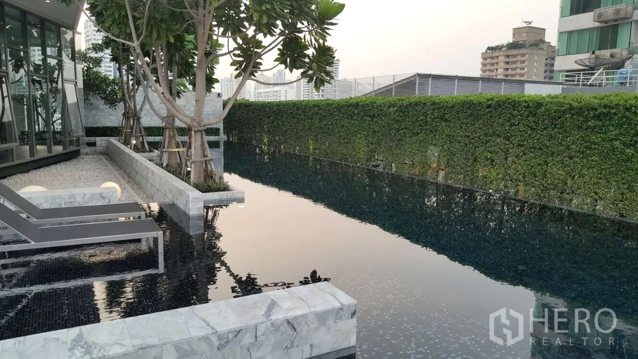 Condominium for rent in Watthana, Bangkok - Leafy lap pool with marble deck, sun loungers and hedge wall at a modern Bangkok condominium.
