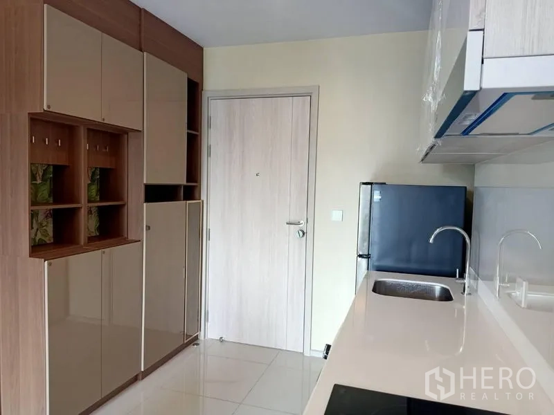 Condominium for rent in Pathum Wan, Bangkok - Entry corridor and kitchen with glossy storage cabinets, sink and refrigerator.