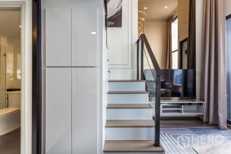 Condominium for rent or sale - Modern staircase with glass railing beside the bathroom entrance and TV cabinet.