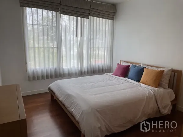 Condominium for rent in Pathum Wan, Bangkok - Corner master bedroom with large windows, white bedding and warm wood floors in a Pathum Wan condominium.