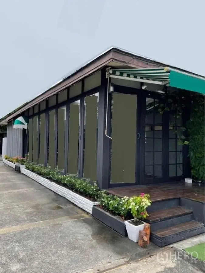 零售空间 出租在Watthana, Bangkok - 临街单层店铺，整面玻璃立面、条纹雨篷与带花箱的小平台。