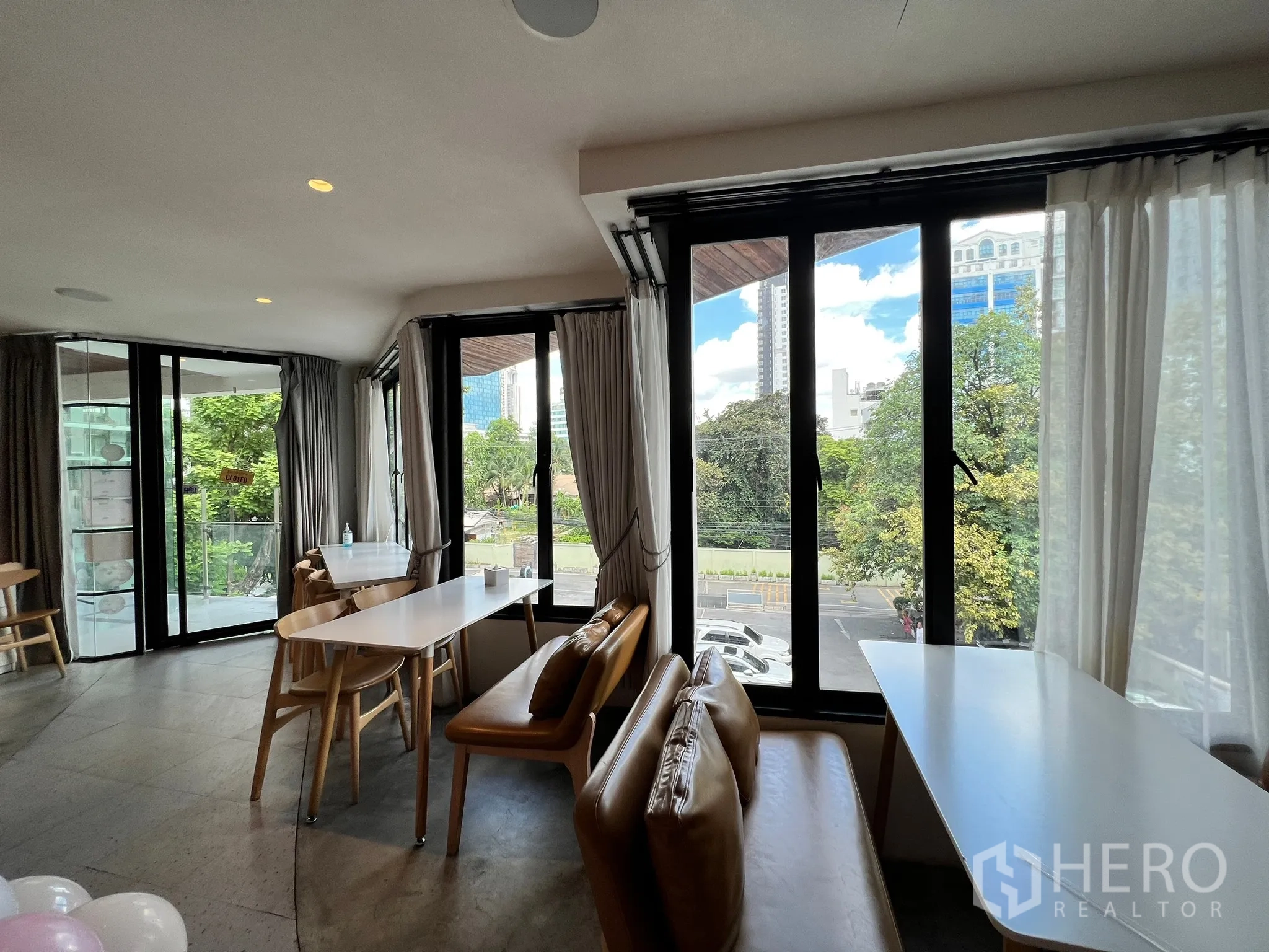 零售空间 出租在Watthana, Bangkok - 靠落地窗的休闲座位，可观绿树与曼谷天际线景观。