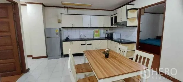 คอนโด ให้เช่าในKhlong Toei, Bangkok - ครัวแบบเปิดตู้สีขาว ผนังกระเบื้อง พร้อมโต๊ะทานอาหารไม้ ติดทางเข้าห้องนอน