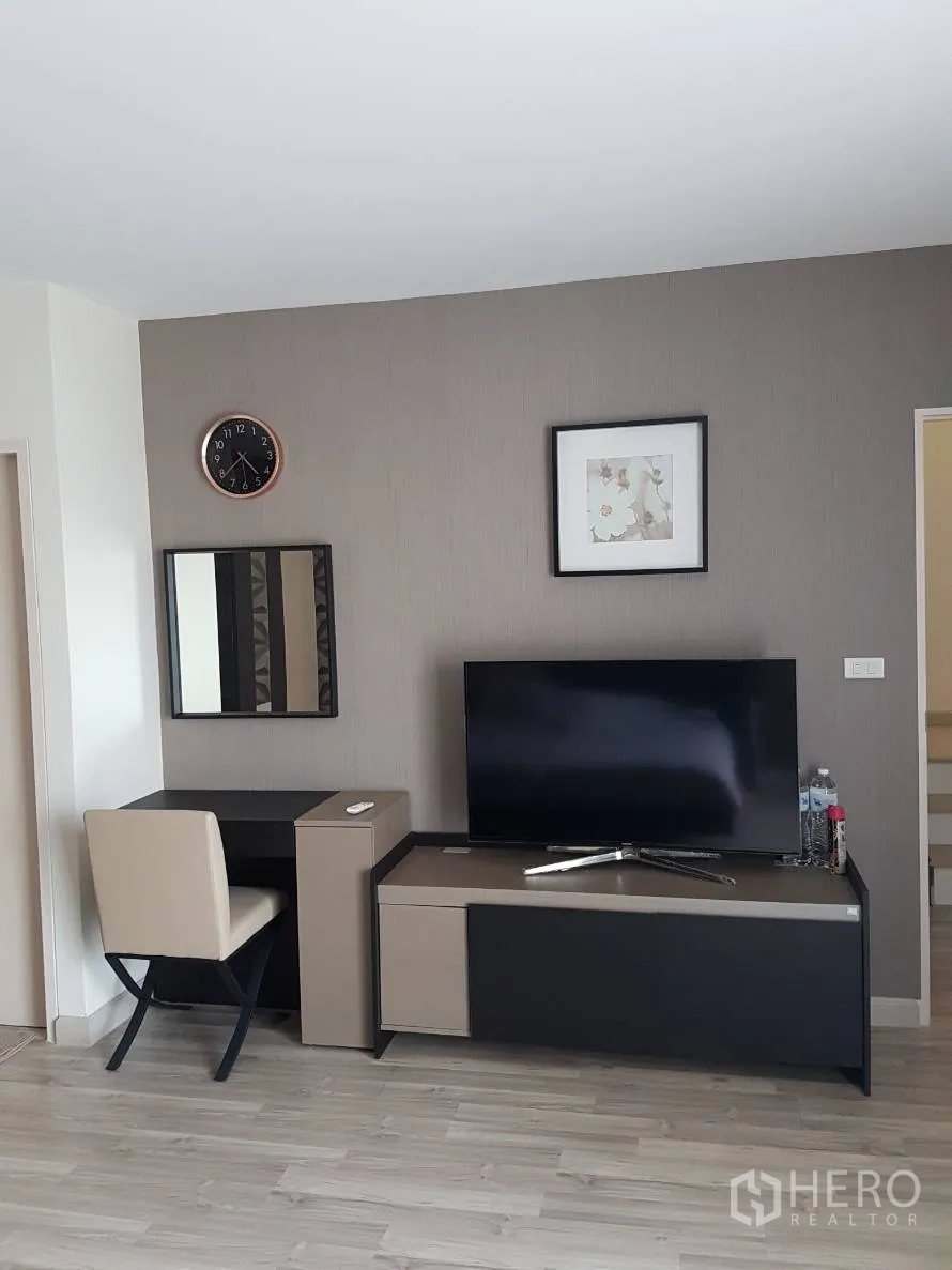 Townhouse for rent or sale in Saphan Sung, Bangkok - Bedroom corner with TV stand, work desk, wall clock and neutral decor.