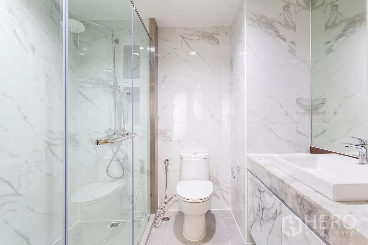 Condominium for rent or sale in Watthana, Bangkok - Modern bathroom with glass shower enclosure, rain shower and marble tiles.