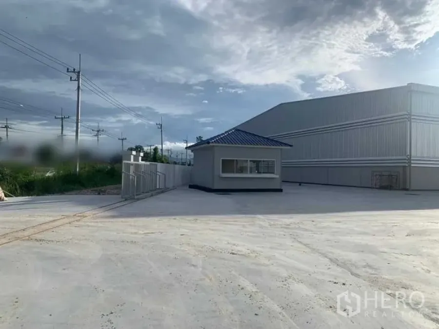Warehouse for rent in Ban Bueng, Chon Buri - Gated entrance with a security guardhouse and perimeter wall beside the warehouse complex.