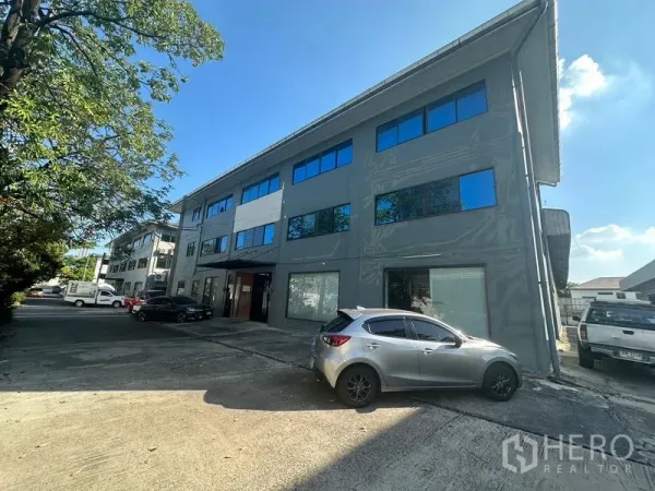 Warehouse for rent in Saphan Sung, Bangkok - Three-storey warehouse building exterior with parking area and trees.
