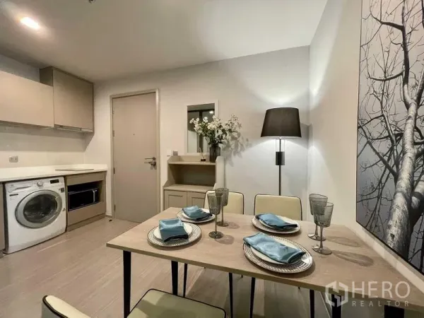 公寓 出租在Chatuchak, Bangkok - 现代公寓内的紧凑厨房，含洗衣机、吊柜与四人餐桌。