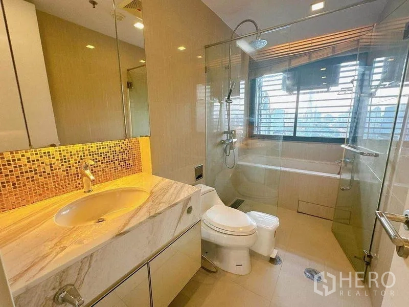 Condominium for rent in Ratchathewi, Bangkok - Contemporary bathroom featuring marble vanity, glass-enclosed shower, and bathtub with warm lighting.
