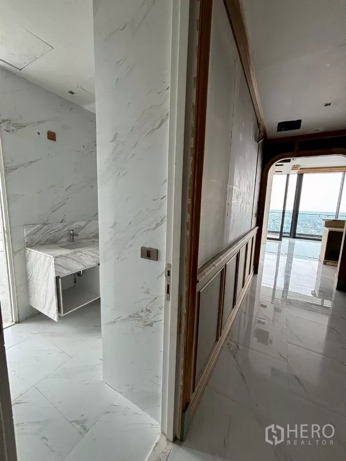 Condominium for sale in Bang Kho Laem, Bangkok - Hallway with marble cladding leading to a bathroom and bright living area overlooking the river.