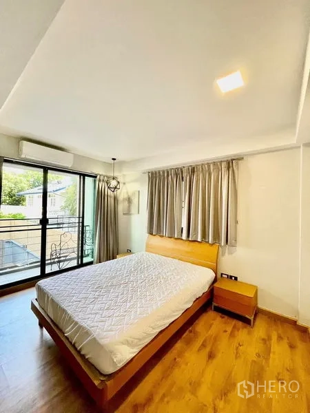 Townhouse for rent in Khlong Toei, Bangkok - Sunlit bedroom with wood floor, bed, and sliding doors to a balcony.