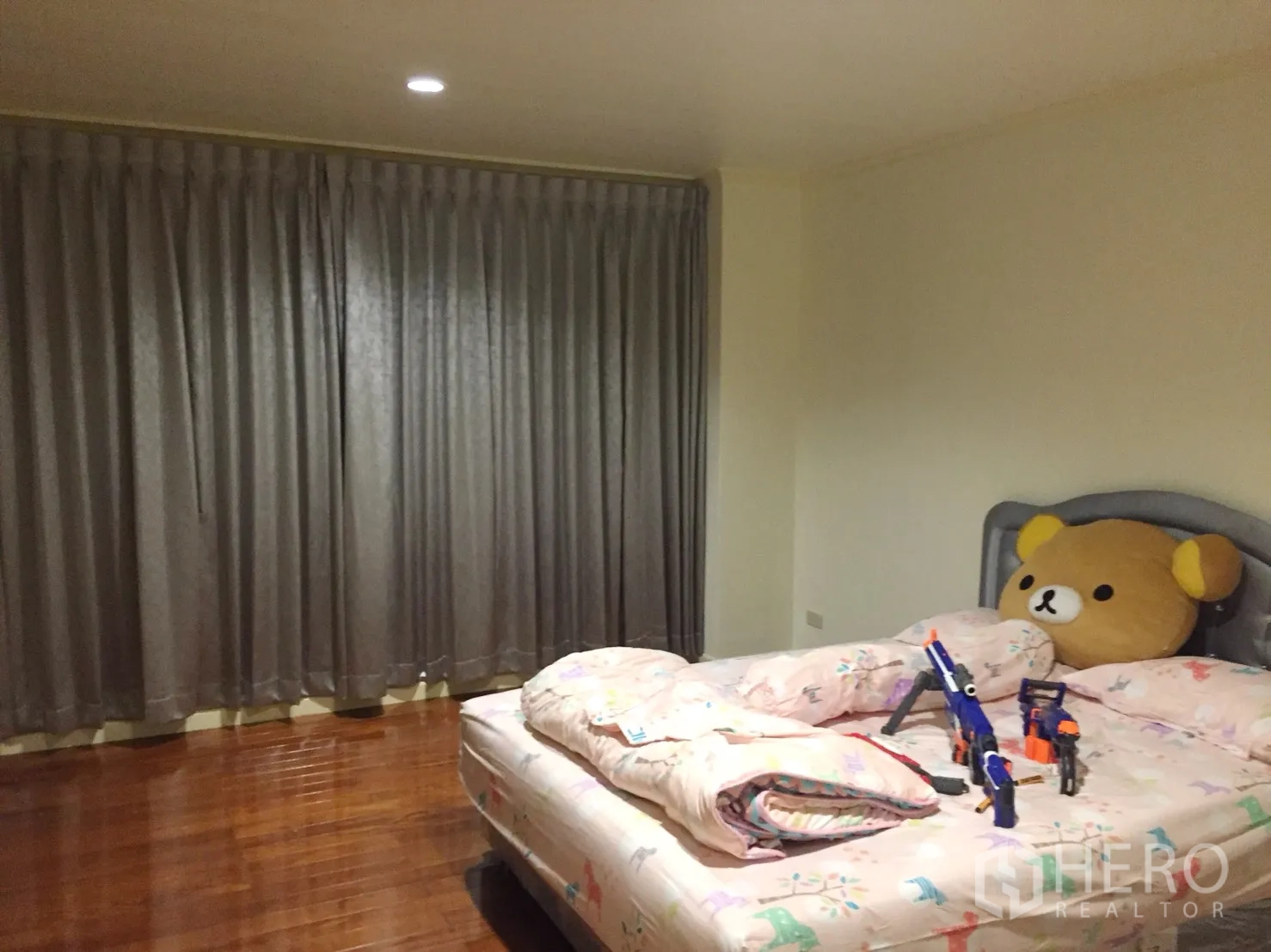 Condominium for rent in Watthana, Bangkok - Cozy bedroom with polished wooden flooring, gray blackout curtains, and a large bed.