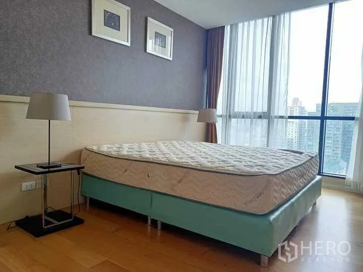 คอนโด ให้เช่าในWatthana, Bangkok - ห้องนอนใหญ่พร้อมเตียงขนาดใหญ่ โคมไฟหัวเตียง และวิวเมืองผ่านหน้าต่างกระจกเต็มบาน.