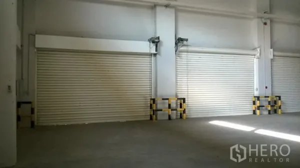 Warehouse for rent in Bang Sao Thong, Samut Prakan - Close-up of interior roller shutters with protective bollards along the wall.