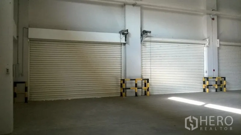Warehouse for rent in Bang Sao Thong, Samut Prakan - Close-up of interior roller shutters with protective bollards along the wall.