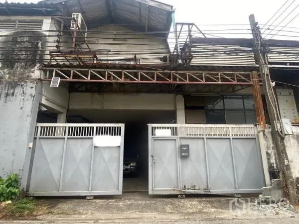 Warehouse for rent or sale in Suan Luang, Bangkok - Street-facing warehouse exterior with wide sliding metal gates, overhead steel truss and utility lines in Suan Luang, Bangkok.