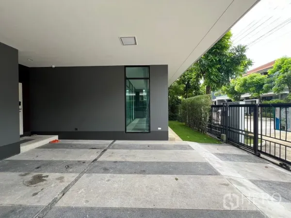 Detached House for rent in Bang Kapi, Bangkok - Covered carport with striped concrete floor and black gate beside a tall window.