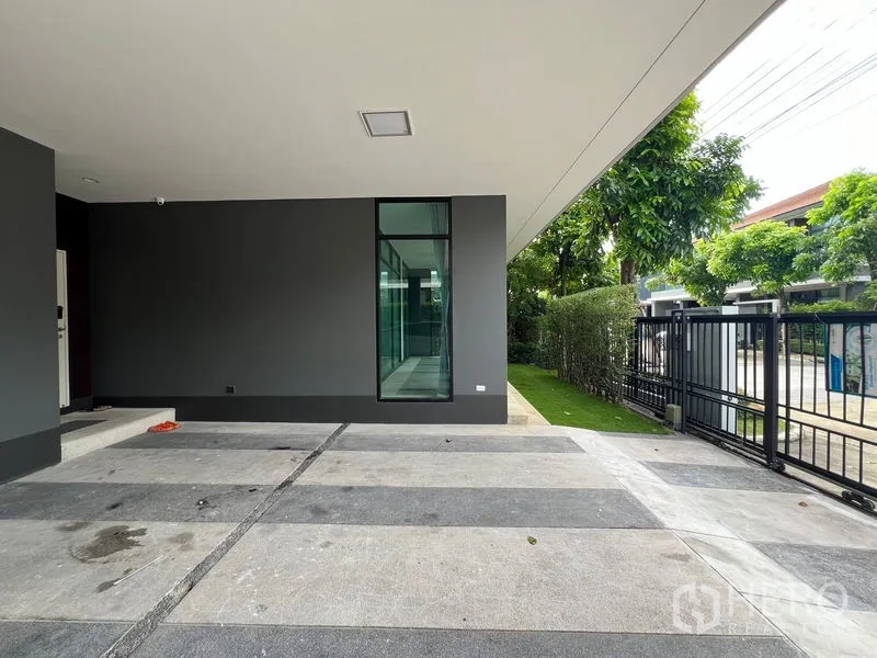 Detached House for rent in Bang Kapi, Bangkok - Covered carport with striped concrete floor and black gate beside a tall window.