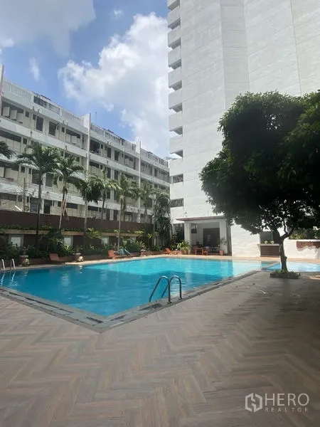 Condominium for rent - Condominium outdoor swimming pool with palm trees, sundeck and surrounding residential buildings under blue sky.