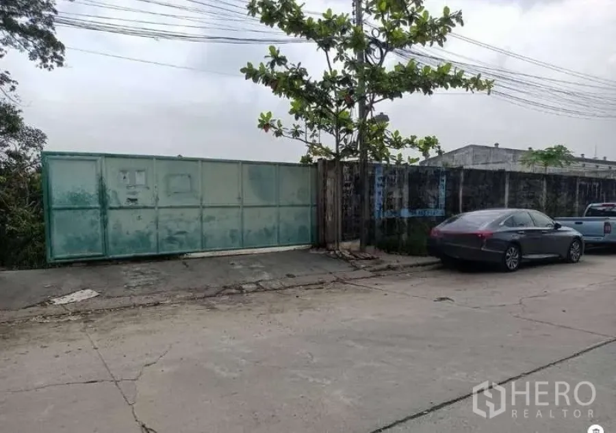 Land for rent in Lat Krabang, Bangkok - Street frontage showing a wide sliding metal gate and parked cars at the entrance to the land.
