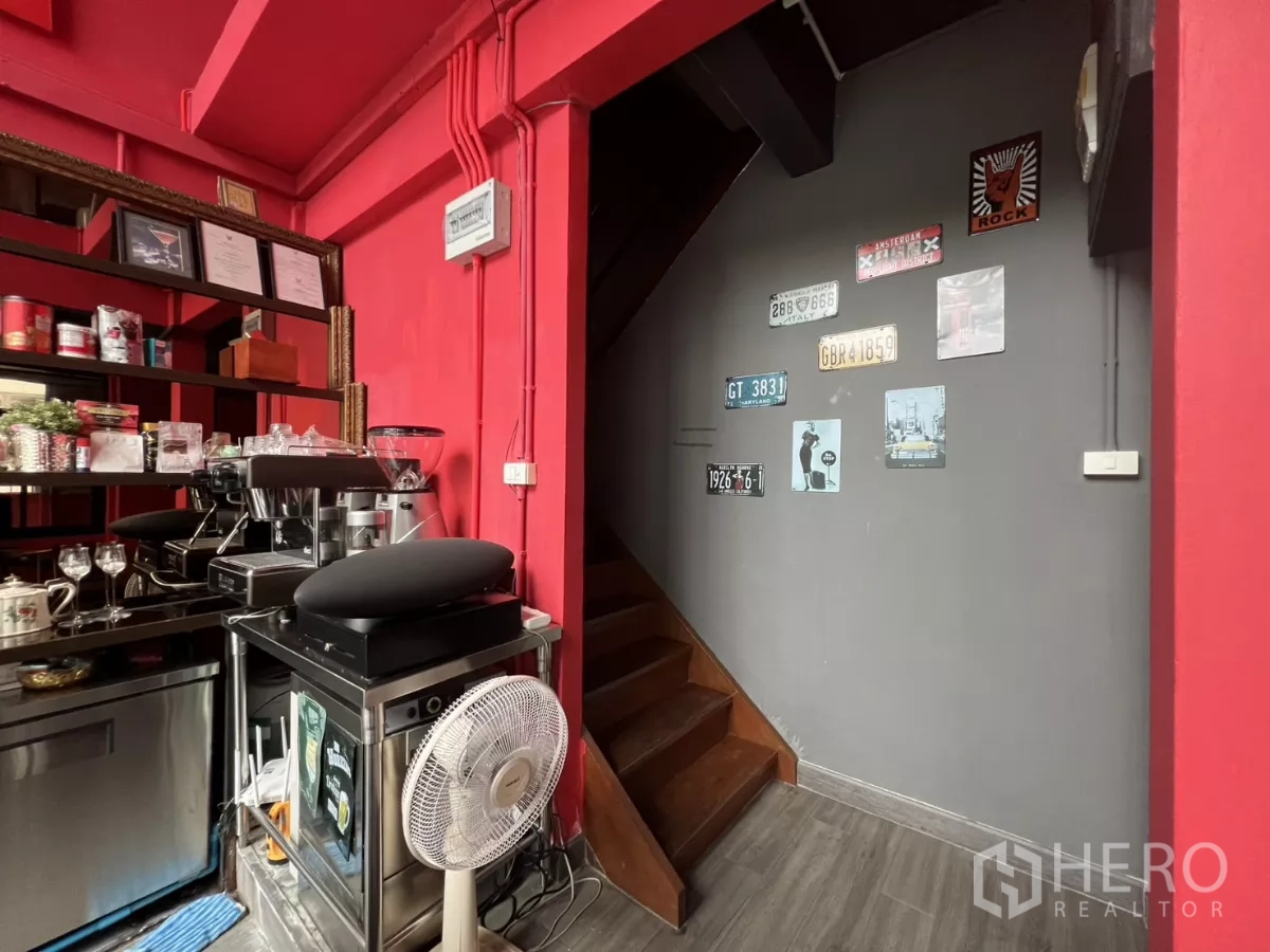 零售空间 出租在Watthana, Bangkok - 咖啡设备与楼梯区域，墙面装饰复古牌照。