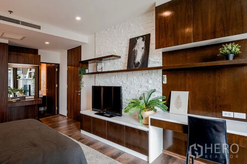 公寓 出售在Khlong Toei, Bangkok - 卧室内电视与书桌区，深色木柜搭配白色砖墙装饰。