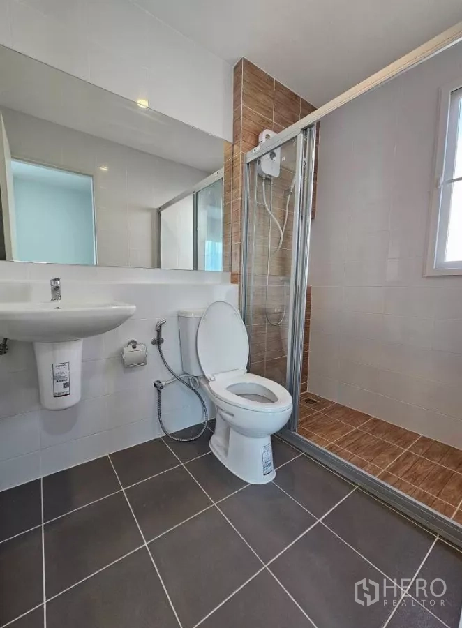 Detached House for rent in Bang Phli, Samut Prakan - Bathroom with glass shower enclosure, toilet, large mirror and tiled floor.