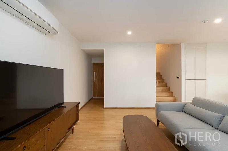 Condominium for rent in Phra Khanong, Bangkok - Living area with TV unit, sofa and entry to staircase on warm wooden floors.