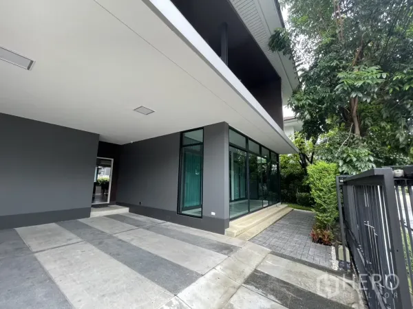 Detached House for rent in Bang Kapi, Bangkok - Wide carport and glass corner wall leading to a garden path with trees.