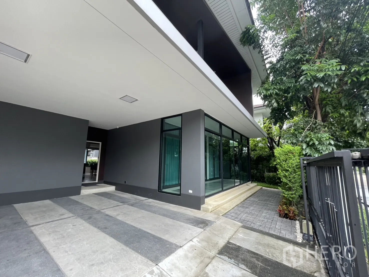Detached House for rent in Bang Kapi, Bangkok - Wide carport and glass corner wall leading to a garden path with trees.