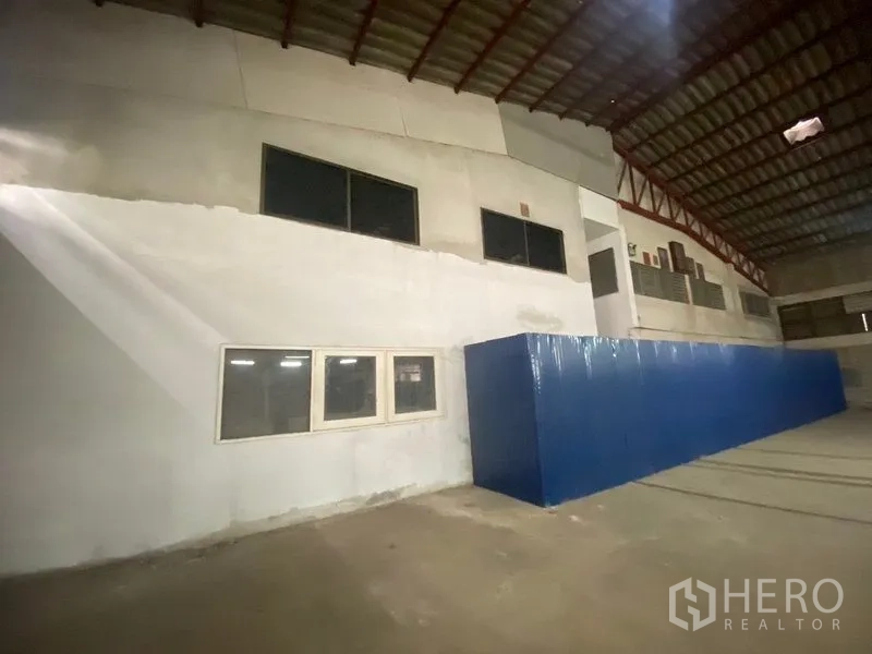Warehouse for rent or sale in Suan Luang, Bangkok - Back wall view with single blue door, high windows and open loading area under a metal roof.