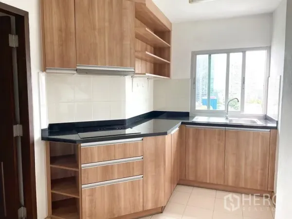 คอนโด ให้เช่าในKhlong Toei, Bangkok - ครัวมุมรูปตัวยู ตู้ไม้ ท็อปหินสีดำ เตาไฟฟ้า และหน้าต่างเหนืออ่างล้างจาน