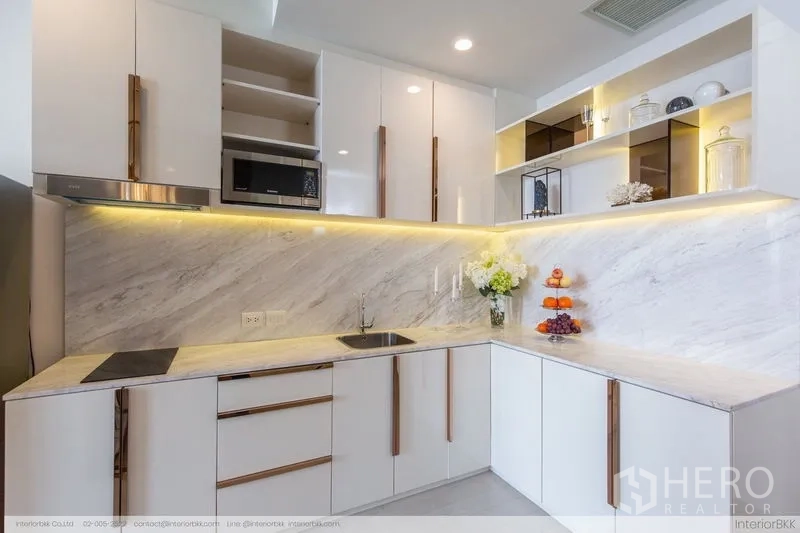 Condominium for rent in Pathum Wan, Bangkok - White L-shaped kitchen with marble backsplash, under-cabinet lighting and open shelving.