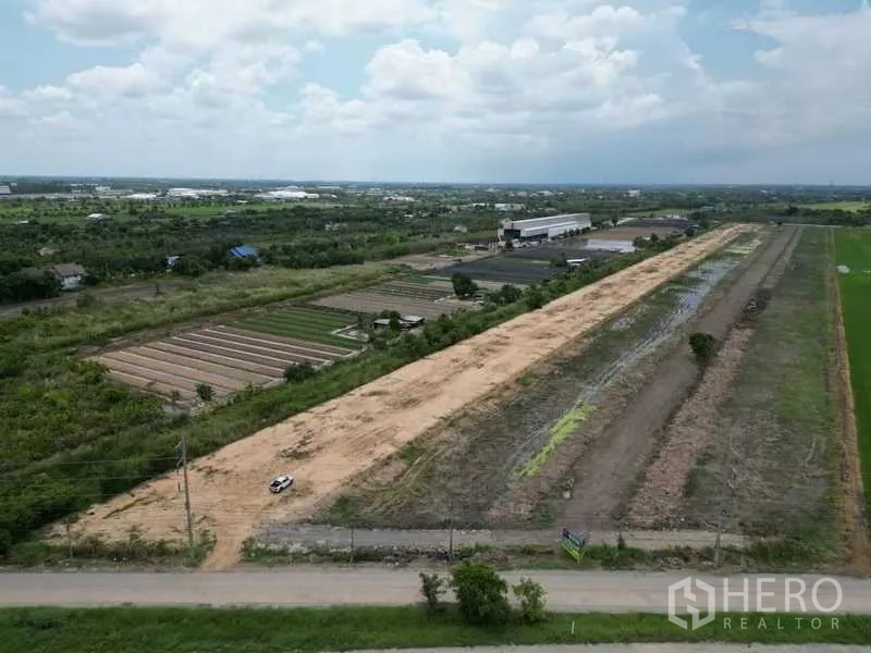Land for sale in Sai Noi, Nonthaburi - Aerial view of a long rectangular land plot with road frontage, level soil, and neighboring farms and a warehouse in Sai Noi, Nonthaburi.