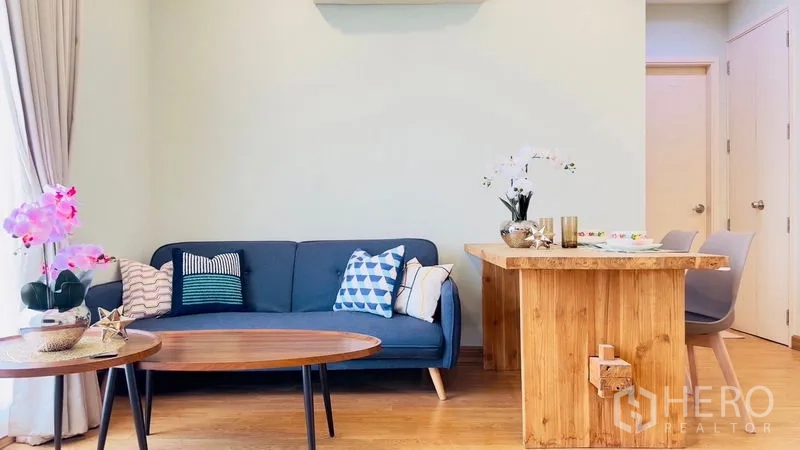 คอนโด ให้เช่าในWatthana, Bangkok - ห้องนั่งเล่นพร้อมโซฟาสีน้ำเงิน โต๊ะกาแฟไม้ แจกันดอกไม้ และเคาน์เตอร์ทานอาหาร