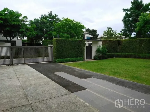 独立式住宅 出租或出售在Mueang Nonthaburi, Nonthaburi - 带金属大门的车道，绿篱环绕与宽阔前庭草地。